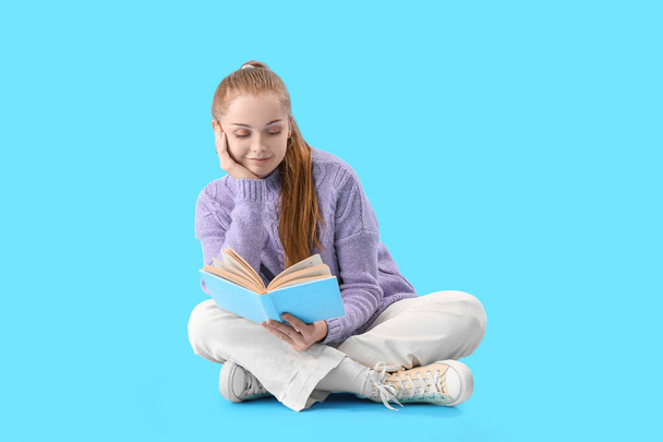 Νεαρή γυναίκα διαβάζει βιβλίο για το μπλε φόντο - Φωτογραφία, εικόνα