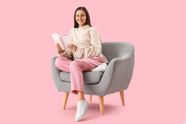 Beautiful woman with book sitting in armchair on pink background - Foto, Imagem