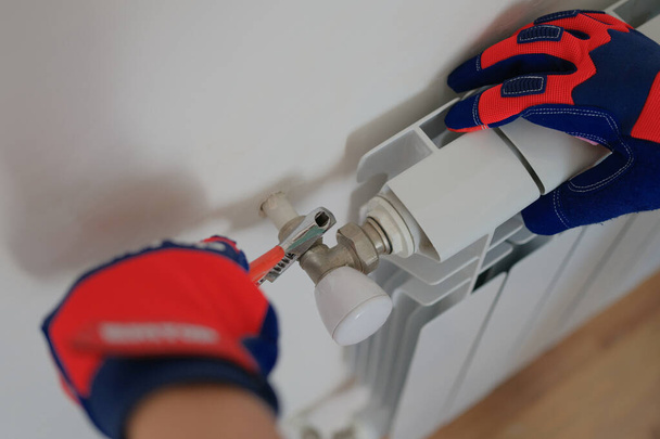 Close-up of man plumber installing heating radiator in apartment or house. Builder installs hot water central heating system. Repair concept - 写真・画像