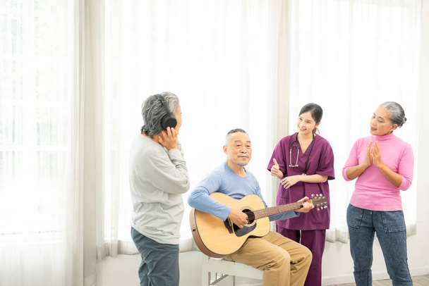 Група людей похилого віку насолоджується діяльністю разом з лікарем. Літні люди мають веселу концепцію. Щасливі старшокласники грають на гітарі та співають пісні, розважаючись разом
. - Фото, зображення