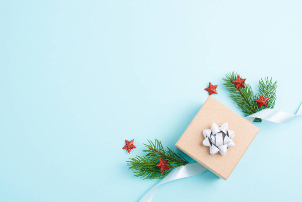 Tarjeta de felicitación navideña con caja de regalo pequeña, estrellas, ramas de cinta y abeto, fondo azul  - Foto, Imagen