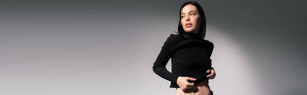 young and trendy woman in black sweater looking away on grey background, banner - Foto, imagen