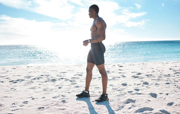 朝にランニングから休憩したり、ビーチでジョギングをしたりする若い無気力な黒人男性に合わせて運動をしてください。彼の心臓と持久力のワークアウトを探している強力な筋肉の男性選手. - 写真・画像
