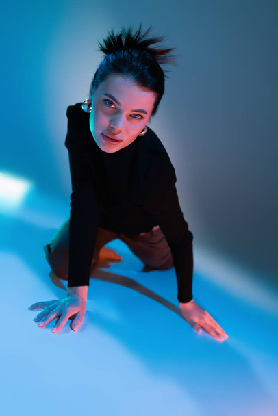 sensual brunette woman in black sweater looking at camera while posing on blue background - Φωτογραφία, εικόνα