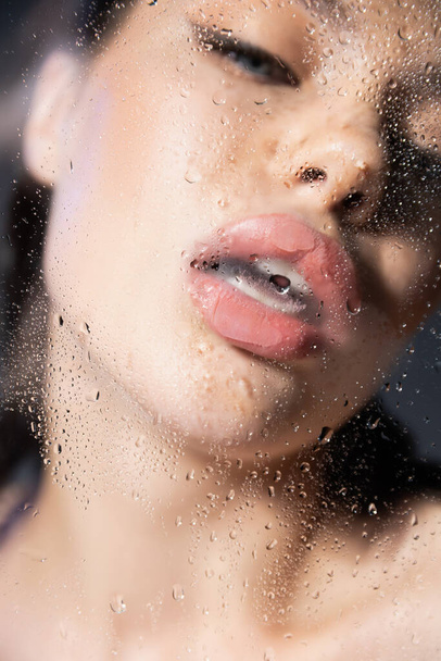 Blurred young woman with opened mouth near wet glass on grey background  - Foto, imagen