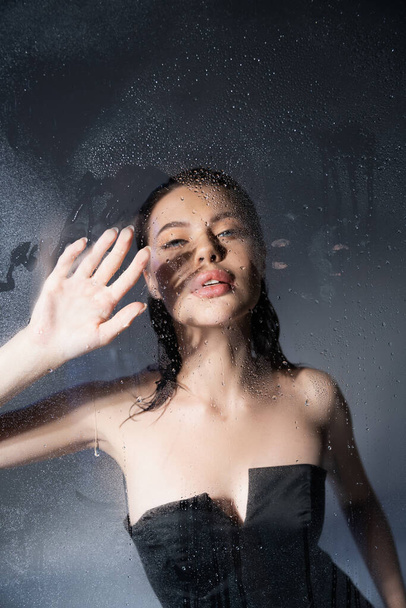 Trendy brunette model in corset touching wet glass on grey background  - Фото, зображення