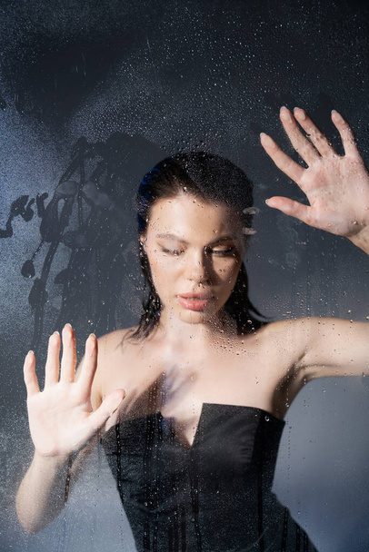 Sexy young model in corset touching wet glass on grey background  - Foto, Bild
