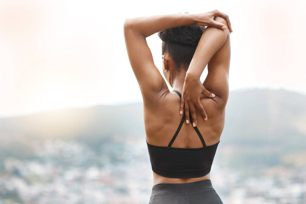 Rearview shot of a young african american female athlete looking at a view while stretching before exercising outside workout. Dedicated black woman warming up before starting her outdoor workout. - Foto, Bild