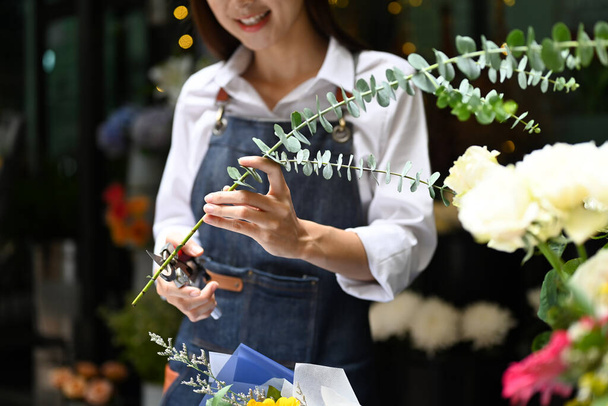 Uśmiechnięta młoda kobieta kwiaciarnia cięcia gałęzi, tworząc piękny bukiet z różnych kwiatów. - Zdjęcie, obraz
