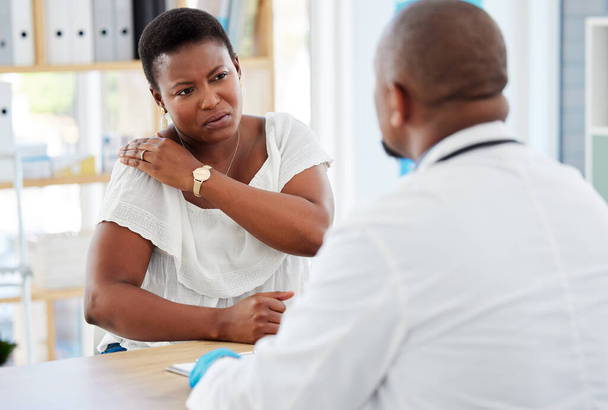 Γυναίκα που δείχνει στο γιατρό της τον τραυματισμό στον ώμο. Αφροαμερικανή ασθενής σε μια γνωμάτευση για τον πόνο στον ώμο της. Γιατρός σε τσεκάπ με ασθενή για πόνο στους ώμους. Γιατρός και ασθενής στην κλινική. - Φωτογραφία, εικόνα