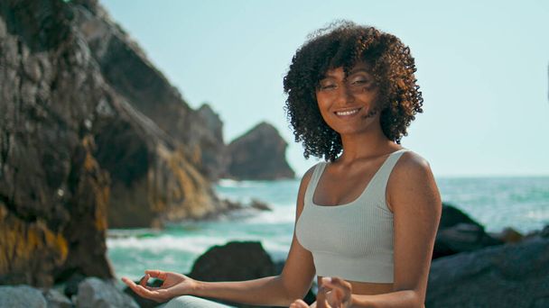 Pretty woman looking camera sitting lotus pose on stone Ursa beach closeup. Relaxed young girl smiling meditation on nature alone. Attractive sportswomen feeling peace harmony practicing yoga outdoors - Photo, Image
