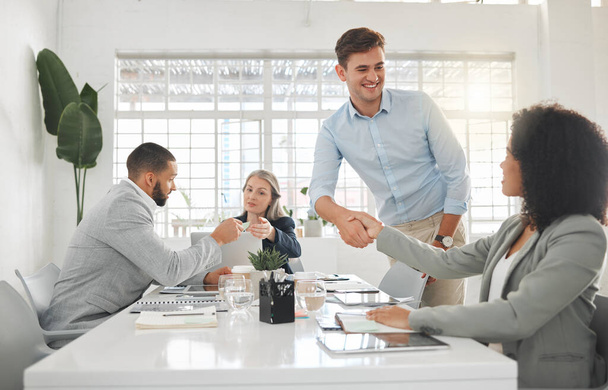 Diverse group of businesspeople having a meeting together at a table at work. Business professionals talking and planning in an office. Young caucasian businessman greeting a mixed race businesswoman. - Photo, Image