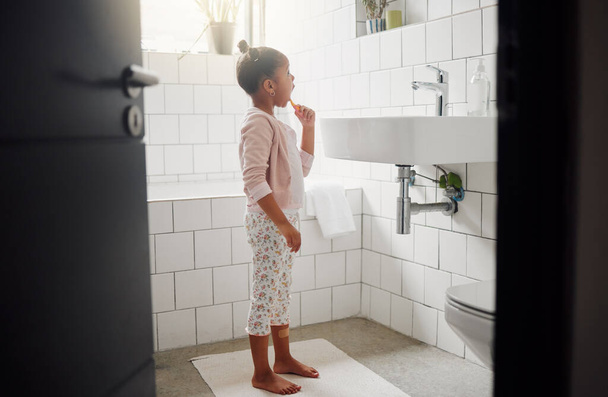 Een gemengd ras schattig klein meisje poetsen haar tanden in een badkamer thuis. Een gelukkig Latijns-Amerikaans kind met gezonde dagelijkse gewoonten om gaatjes te voorkomen en emaille te versterken. - Foto, afbeelding