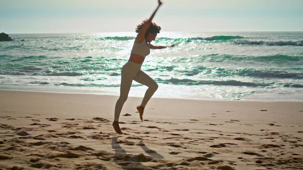 Menina ativa feliz fazendo elementos de ginástica na frente belas ondas do oceano manhã ensolarada. Mulher esportiva magro realizando rodas de papelão na praia de areia Ursa. Esportista alegre se exercitando na praia. - Foto, Imagem