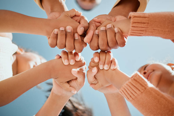 View from below of young mixed race family holding hands and forming a circle while standing together against a blue sky. Parents and children saying prayer showing support and teamwork. - Foto, Imagem