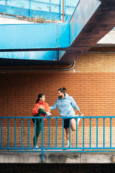 Jongeman en zijn vrouwelijke vriend dragen sportkleding die zich uitstrekt na het rennen tijdens regenachtige dagen en glimlachend. - Foto, afbeelding