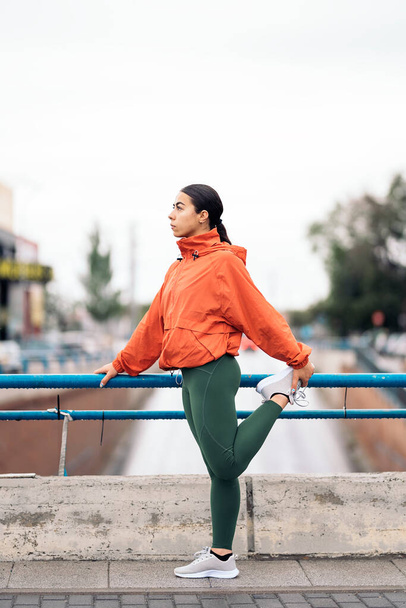 Young active woman wearing sports clothes looking at front and stretching after running in the city during rainy day. - Фото, зображення