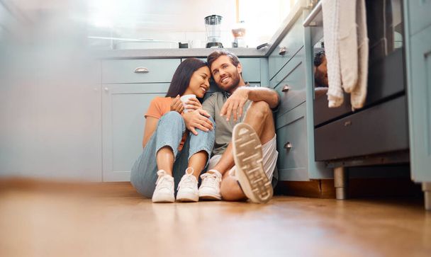 Young happy interracial couple bonding while drinking coffee together at home. Loving caucasian boyfriend and mixed race girlfriend sitting on the kitchen floor. Cheerful husband and wife relaxing an. - Fotografie, Obrázek