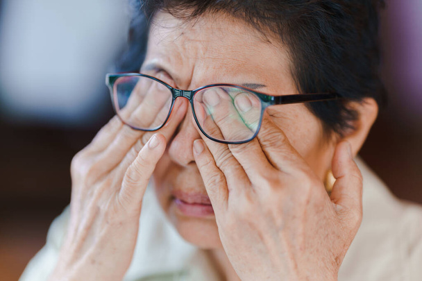 Vanhempi nainen käyttää silmälaseja ja hieroo silmiään käsillään väsymyksen vuoksi. Iäkkäiden terveysongelmien käsite. - Valokuva, kuva