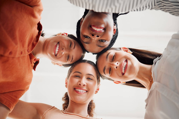 Portrait of happy businesswomen joining their heads together in a circle in an office at work. Diverse group of cheerful businesspeople having fun standing with their heads together in unity. - Photo, Image