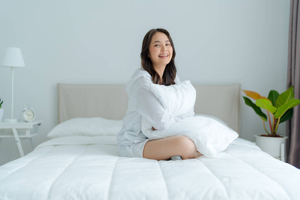 Una hermosa mujer sentada sobre una almohada en su dormitorio, sonriendo, riendo felizmente. con una cara brillante - Foto, Imagen