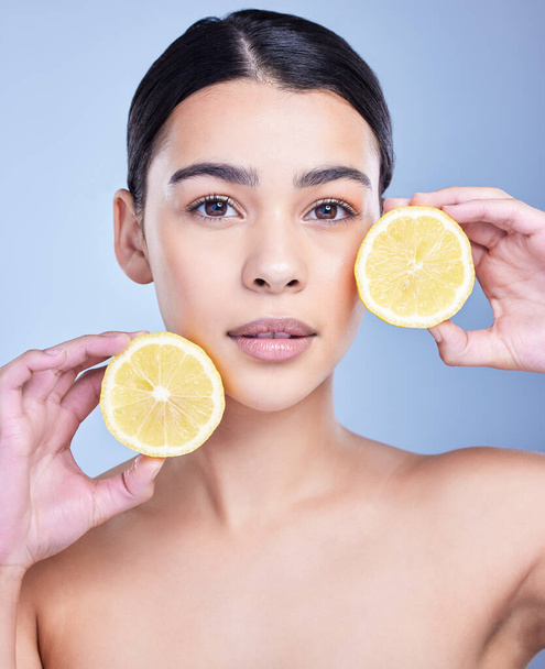 Estudio Retrato de una hermosa joven mestiza sosteniendo un limón. Modelo hispana usando un limón para iluminar su piel sobre un fondo de copyspace azul. - Foto, imagen