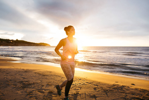 Junge Frau in Sportkleidung joggt bei Sonnenaufgang am Strand - Foto, Bild