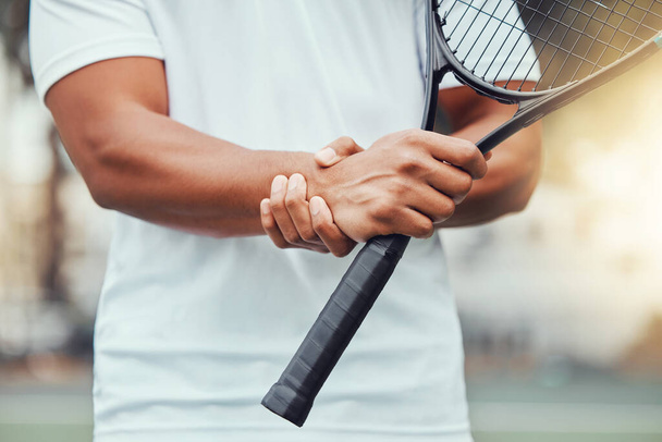 Closeup of unknown indian tennis player suffering from wrist injury in court game. Ethnic fit professional in pain while holding and rubbing hand after match. Sporty man holding racket in sports club. - Φωτογραφία, εικόνα
