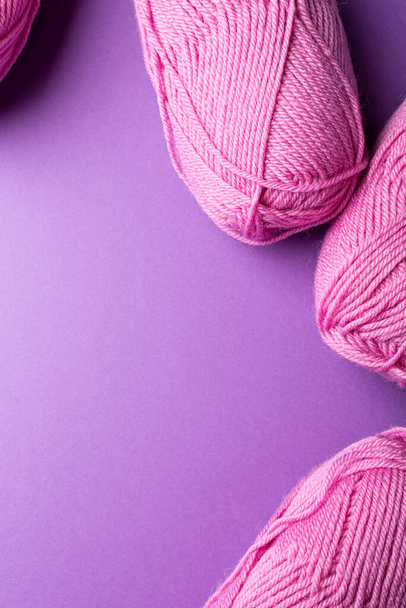 Knitting background with pink wool yarn balls over lilac, top view, flat lay with copy space - Foto, afbeelding