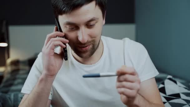 Male holds pregnancy test and happily calls friend to tell him good news, he is going to be father. Happy man calling to tell her she is pregnant, we are going to be parents. Guy is happy pregnancy.  - Footage, Video