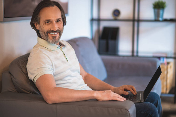 Work from home. Good-looking mature man sitting on a sofa with a laptop - Foto, Imagem