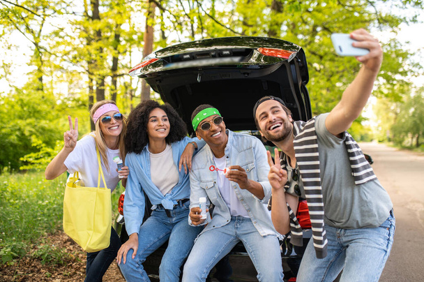 Selfie together. Group of friends making selfie in the forest while sitting on the car boot - Φωτογραφία, εικόνα