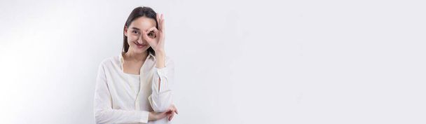 Close up portret atrakcyjne osobliwe młoda kobieta co lornetka z rąk pokazując ok gest na białym tle studio. - Zdjęcie, obraz