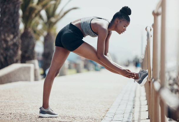 Fitness, running and black woman stretching legs outdoors to start marathon training, cardio exercise or urban city sports workout in Brazil. Strong, focus and runner athlete warm up of body wellness. - Foto, Imagen