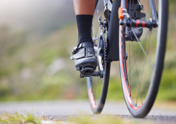 Closeup of one woman cycling outside. Sporty fit female athlete with her feet on bicycle pedals while riding a bike on a road for exercise. Endurance and cardio during a workout and training. - Photo, image