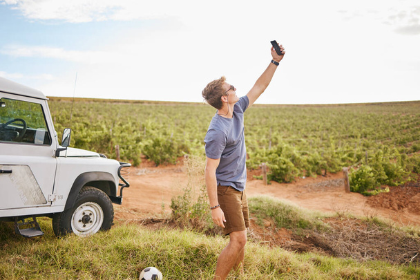 Phone selfie, travel and car road trip nature of a man using a mobile outdoor on a drive break. Countryside, summer vacation and person using technology near a agriculture farm and motor transport. - Zdjęcie, obraz