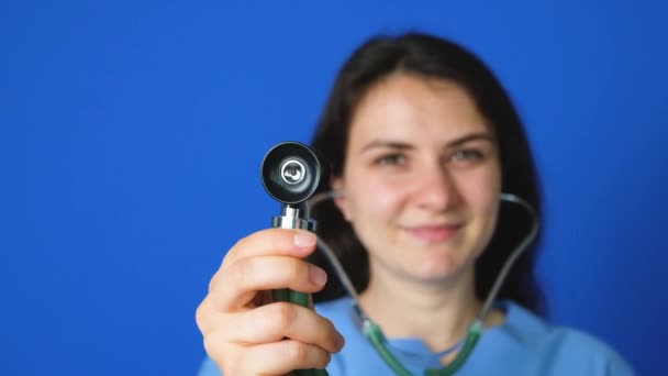 Lääkäri tai sairaanhoitaja, jolla on stetoskooppi, hymyilee sinisellä taustalla - Materiaali, video