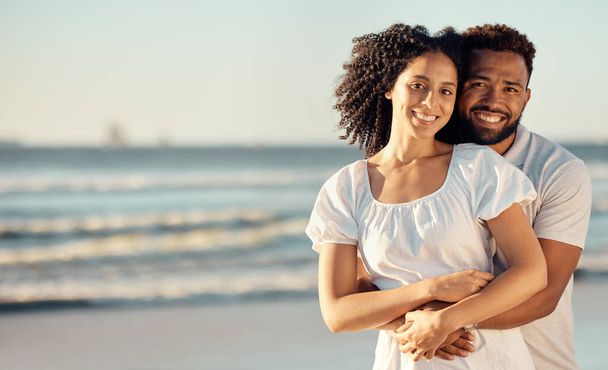 Closeup portrait of an young affectionate mixed race couple standing on the beach and smiling during sunset outdoors. Hispanic couple showing love and affection on a romantic date at the beach. - Fotografie, Obrázek