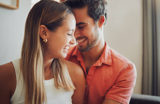 Close up of funny young caucasian couple touching heads laughing and looking happy to be together while spending time at home. Loving smiling boyfriend embracing girlfriend from behind. - Photo, image