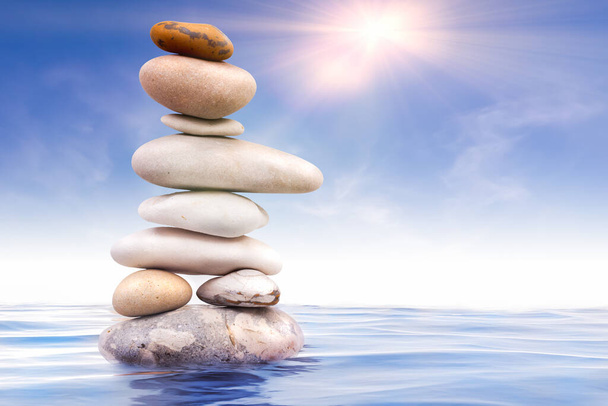 Piedras Zen equilibradas en el agua con el cielo azul y los rayos de sol de la mañana - Foto, Imagen