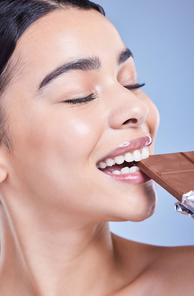 Egy gyönyörű vegyes fajú nő kezében egy tábla csokoládéval. Spanyol modell snacking desszert ellen kék copyspace háttér. - Fotó, kép