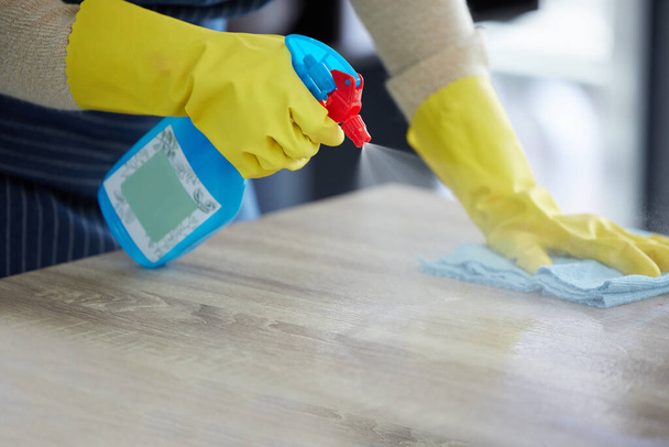 Handen, handschoenen en sproeitafel met ontsmettingsmiddel voor schoon huis. Keuken teller, veiligheid thuis en desinfectie met alcohol oplossing in fles om thuis te beschermen tegen ziektekiemen, stof en bacteriën - Foto, afbeelding