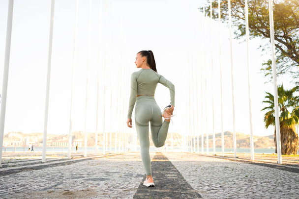 Woman Stretching And Warming-Up Legs Before Running. Fit sport woman stretching her body warm up before workout outdoor. Girl in sportswear exercises outside in summer park for health and wellbeing. - 写真・画像
