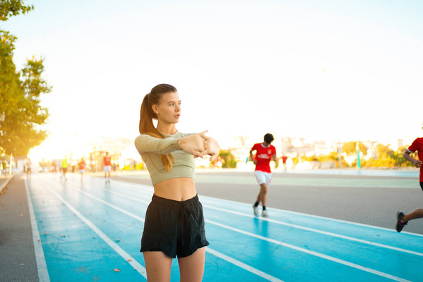 Woman Stretching And Warming-Up Arms Before Running. Fit sport woman stretching her body warm up standing on Running track start line ready jogging. Athletic woman prepare for running training - Foto, Imagem