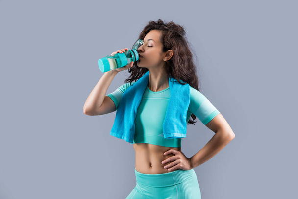 fitness woman with sport towel drinking water in studio. fitness woman hold sport towel drinking water isolated on yellow background. fitness and sport. - Photo, image
