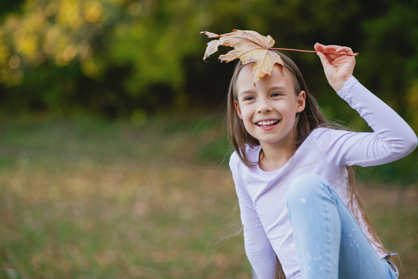 Симпатична дівчинка тримає жовтий кленовий лист над головою
. - Фото, зображення