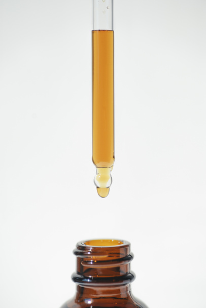 A drop of liquid falling from a pipette into an amber bottle. Skincare products, natural cosmetic on white background. Beauty concept for face and body care. - Valokuva, kuva