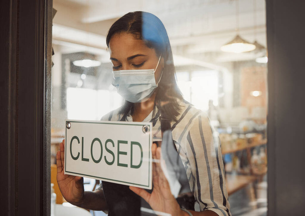 Businesswoman closing her shop in the pandemic. Business owner hanging a closing sign in her shop entrance. Small business owner closing her store in covid lockdown. Boss wearing a mask in her store. - Photo, Image
