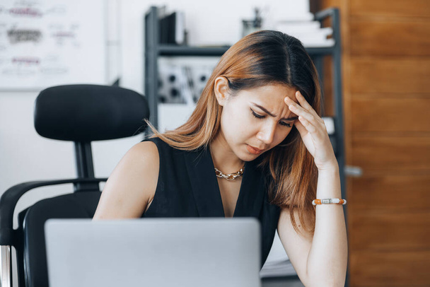 Beautiful Asian woman working in an office, she is a businesswoman who owns a company, she has a headache due to long and large paperwork leaving her tired and dizzy. The concept of sickness from work - Foto, imagen