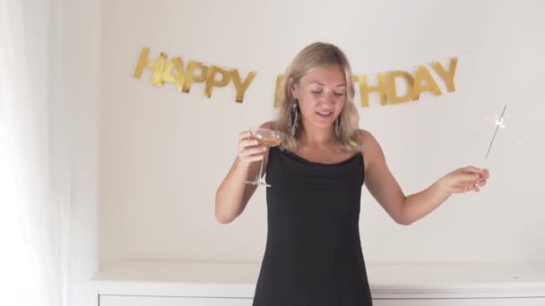 Μια όμορφη γυναίκα με ένα ποτήρι κρασί και μια σπίθα στα χέρια της γιορτάζει τα γενέθλιά της στο σπίτι μόνη της. - Πλάνα, βίντεο